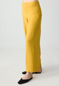 Gele linnen broek met brede benen en een rechte pasvorm, voorzien van een schone tailleband en een zijrits. Gemaakt in combinatie met zwarte puntige flats.