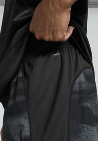 Svarta sportshorts med ett ventilerande tyg, texturerad midjeband och en glansig sidopanel med ett subtilt mörkt mönster. DRYCELL-logotyp tydlig.