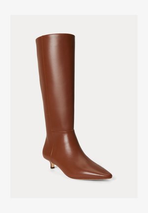 Stivale alto marrone in pelle fino al ginocchio con punta appuntita e tacco basso kitten su uno sfondo chiaro uniforme.