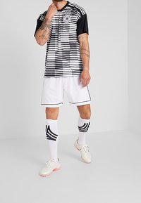 Camiseta de fútbol a rayas blancas y negras con mangas cortas, acompañada de pantalones cortos blancos y calcetas hasta la rodilla con un patrón negro.