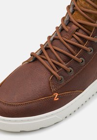 Bruine leren sneaker met een gestructureerde afwerking, leren accent bij de kraag en een lichtgekleurde rubberen zool. Metalen oogjes en bruine veters.