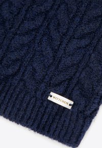 Granatowa dzianinowa czapka z wzorem warkocza; posiada srebrną metkę z wytłoczonym napisem "WITTCHEN" przymocowaną do dolnej krawędzi. Miękka w dotyku.