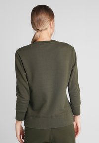 Sudadera de color verde oliva con mangas largas, cuello redondo y puños y dobladillo acanalados. Textura suave, detalles de costura mínimos y corte relajado.