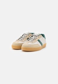 Beige and white sneakers with green accents, rubber sole, suede and canvas materials, featuring lace-up design and logo on tongue.