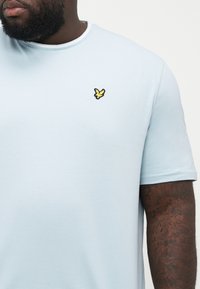Lys blå kortærmet t-shirt lavet af glat bomuld. Har et lille sort og gult broderet logo på venstre bryst.