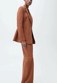 Blazer i hlače u boji rđe izrađeni od teksturirane tkanine. Blazer ima rever i prednje džepove, krojen da osigura uski siluet.