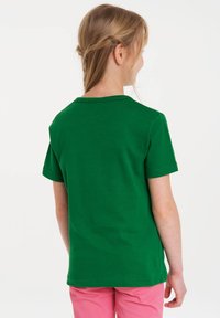 Green cotton T-shirt with a crew neck and short sleeves, displayed from the back, paired with pink pants. Smooth texture, no patterns.