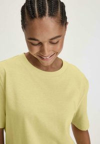 Lichtgele katoenen t-shirt met korte mouwen en een ronde hals. De stof lijkt zacht en soepel, met een ontspannen pasvorm.