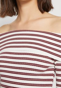 Top off-the-shoulder con righe orizzontali bianche e bordeaux, texture a costine e vestibilità aderente nella parte superiore del corpo.