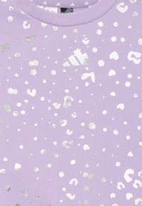 Fialová tkanina s kovovými striebornými roztrúsenými leopardími škvrnami a malým logom Adidas blízko rebrovaného okrúhleho výstrihu.