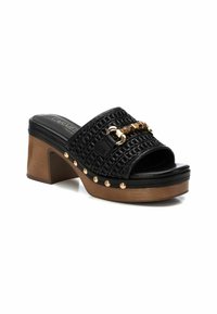 Sandalia deslizante negra de tejido con un tacón de madera grueso, que presenta acentos de cadena dorada y tachuelas decorativas a lo largo de la base. Diseño superior texturizado.