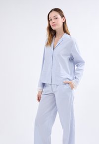 Conjunto de pijama de rayas azul claro con una parte superior con cuello y pantalones largos. La parte superior cuenta con dos bolsillos frontales y un acabado de encaje en las mangas. Tejido suave.