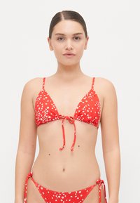 Bikini rouge avec un motif floral, comportant un haut triangulaire avec des liens ajustables et un bas à nouer sur les côtés assorti. Matériau lisse et extensible.