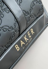 Černá embosovaná syntetická taška s květinovými vzory, lesklým povrchem a zlatým logem. Texturované akcenty zvýrazňují design.