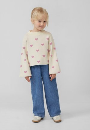 Cremfarbener Pullover mit rosa Herzmustern, weiten Ärmeln, kombiniert mit blauen locker geschnittenen Jeans und weißen Schuhen. Glatte Textur, lässiges Design.