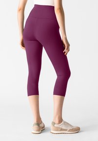 Bordeaux gekleurde cropped leggings met een hoge tailleband, gemaakt van rekbaar materiaal. Draagt met lichtgekleurde sportschoenen. Gladde textuur, strakke pasvorm.