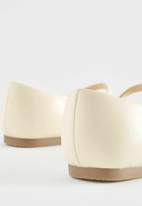 Scarpe flat color crema con una finitura sintetica liscia, retro arrotondato e dettagli di cucitura sottili. Suole in gomma marrone chiaro.