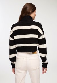 Czarny i biały w paski krótki sweter z wysokim kołnierzem, wykonany z dzianiny, z długimi rękawami. Połączony z jasnoróżowymi dżinsami z tylnymi kieszeniami.