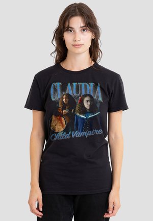 Junge Frau trägt ein schwarzes T-Shirt mit mehreren Bildern eines Mädchens mit lockigem Haar und dem Text "CLAUDIA Kindervampir."