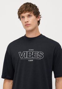 Camiseta oversized de algodón negro con un atrevido estampado gráfico blanco que dice "NO BAD VIBES PLEASE" en el pecho. Manga corta.