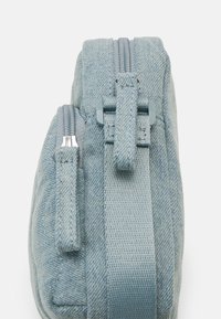 Svetlomodrá textilná taška s textúrovaným povrchom, vybavená zipsom, nastaviteľným popruhom a vzorovanými akcentmi po stranách.