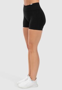 Zwarte rekbare shorts met een hoge tailleband, gemaakt van zachte stof. Heeft een gladde textuur en een slanke pasvorm. Gecombineerd met witte sportschoenen.