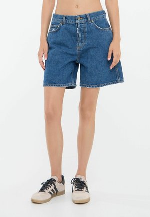Denim šorti vidējā zilo mazgāšanā ar augstu jostu, piecām kabatām un saplēstu apakšu. Apvienoti ar gaiši brūniem sneakers ar melniem akcentiem.