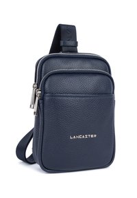 Borsa a tracolla compatta in pelle blu navy con tasca frontale a zip, cerniere argentate e logo "LANCASTER" sul pannello anteriore.