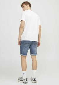 Balta trumpa rankovė t-shirt, mėlyni džinsiniai šortai su sukniuotais kraštais, matomos gale esančios kišenės, baltos kojinės su mėlynomis detalėmis ir pilkos sportbačiai.