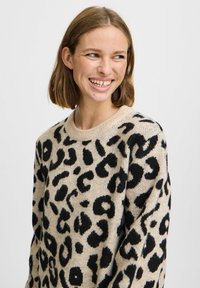 Pull beige avec un motif léopard noir, en tissu tricoté texturé, col rond et manches longues.