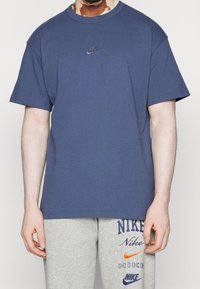 Mörkblå bomulls t-shirt med korta ärmar, rundad halsringning, med en liten broderad Nike-logga på bröstet. Slät textur.