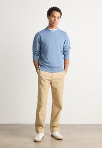 Ανοιχτό μπλε φούτερ από βαμβάκι με ριμπ μανσέτες και στρίφωμα, συνδυασμένο με μπεζ παντελόνι από βαμβάκι και �λευκά αθλητικά παπούτσια με μπεζ λεπτομέρειες.