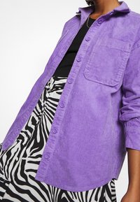 Purple corduroy shirt with button front, collar, and one chest pocket, paired with a black-and-white zebra patterned skirt.