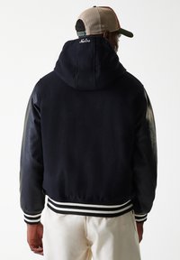 Navy fleece jacket with black leather sleeves, fitted ribbed cuff, and hem. Hooded design features "New Era" logo at the back.