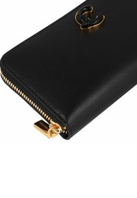 Zwarte leren portemonnee met gouden rits en goud-zwart decoratief embleem op de voorste hoek.