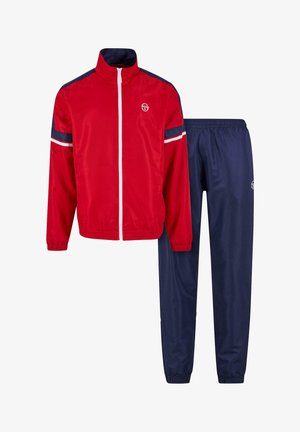 Sarkans sporta mētelis ar augstu apkakli, baltu rāvējslēdzēju un tumši zilu akcentu, apvienots ar tumši zilām sporta biksēm, kuru elastīgā josta un logo.