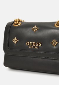 Sort læderhåndtaske med guldlåse, prydet med et guld logo og dekorative metalliske detaljer. Tekstureret overflade med en struktureret form.