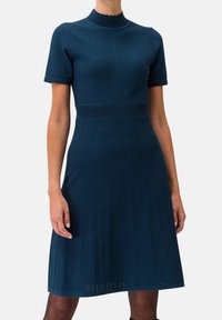 Stickad klänning i mörk teal, med korta ärmar, en scallop-formad halsringning och texturerade vertikala ränder på kjolen. Slät tyg.