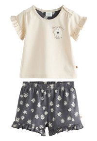 Cremefarbenes Kurzarm-Top mit Rüschenärmeln und floralem Stickmuster, kombiniert mit grauen Shorts, die weiße Gänseblümchenmuster und gerüschte Säume aufweisen.