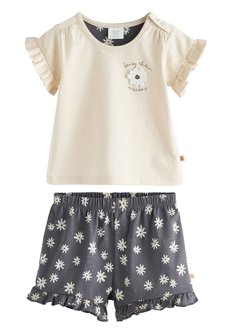 Cremefarbenes Kurzarm-Top mit Rüschenärmeln und floralem Stickmuster, kombiniert mit grauen Shorts, die weiße Gänseblümchenmuster und gerüschte Säume aufweisen.