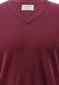 Burgunderfarbener V-Ausschnitt-Pullover aus weichem Stoff mit leicht strukturiertem Finish. Das Etikett trägt die Aufschrift "CARL GROSS BLACK LINE."