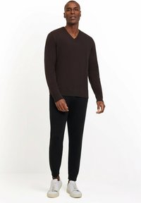 Dunkelbrauner V-Ausschnitt-Pullover kombiniert mit engen schwarzen Hosen und weißen Sneakers. Der Stoff wirkt glatt mit einer taillierten Passform.