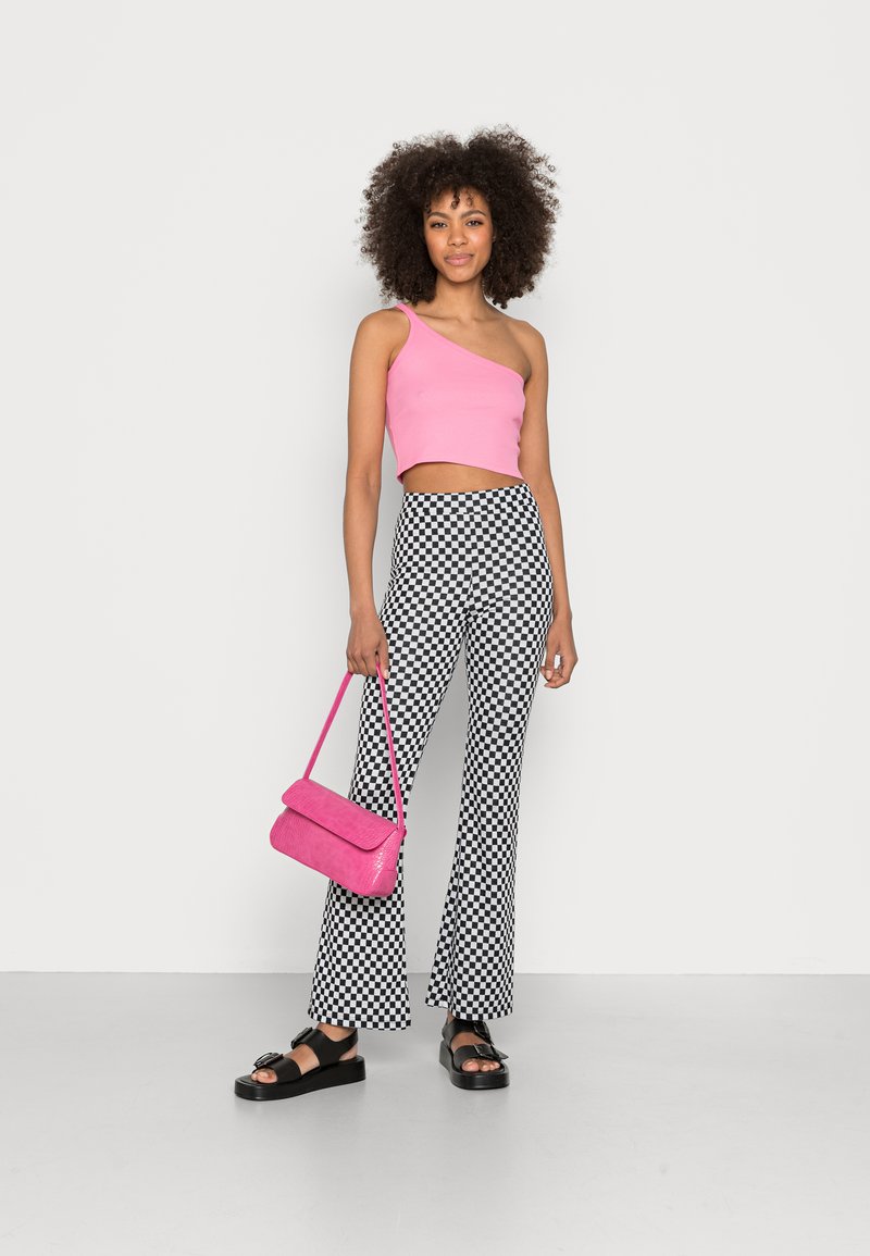 Top cropped rosa de um ombro, combinado com calças flare xadrez preto e branco. Acessórios incluem uma mala de ombro rosa e sandálias de plataforma pretas.