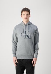 Felpa grigia realizzata in morbido tessuto, con tasca a marsupio e polsini a costine. Sul davanti è presente un audace logo "Calvin Klein Jeans" e le iniziali.
