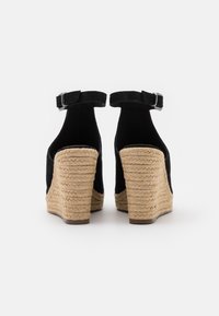 Černé sametové wedge boty na podpatku s texturovanou jutovou platformou, vybavené nastavitelným páskem kolem kotníku a hladkým vnitřním podšíváním.