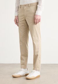 Gaiši brūni kokvilnas chinos bikses ar taisnu piegriezumu, ar pogu aizdari un sānu kabatām, apvienotas ar baltām sporta apaviem un gaiši pelēkām zeķēm.