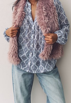 Osoba ubrana w niebieską, wzorzystą, zapinaną na guziki koszulę, jasnoniebieskie dżinsy i trzymająca otwartą mauve kamizelkę ze sztucznego futra.