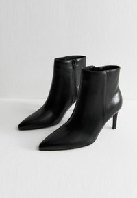 Botas de tobillo de cuero negro con punta afilada y un diseño elegante. Cuentan con un cierre lateral y delgados tacones de aguja para mayor altura.