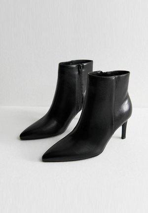 Stivaletti neri in pelle con punte affusolate e design elegante. Presentano una cerniera laterale e tacchi a stiletto sottili per un aumento di altezza.