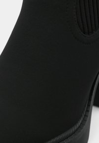 Gros plan sur une botte Chelsea noire montrant un matériau supérieur lisse, un panneau latéral élastique, des coutures et le bord de la semelle texturé.